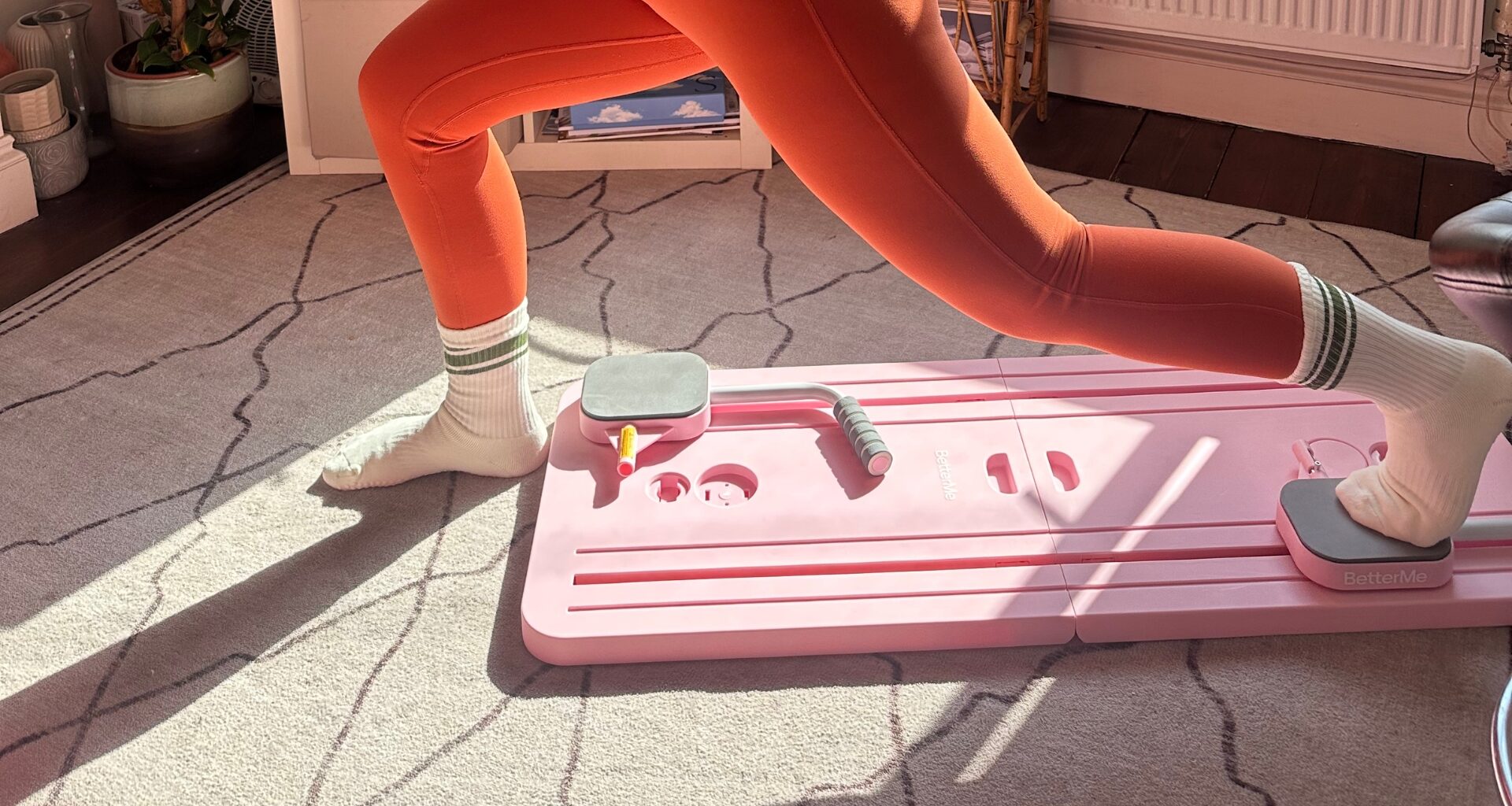Bottom half of person exercising using a Pilates board, with one foot on a slider on the board and the foot behind the person’s front foot