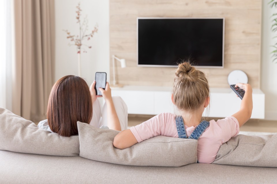 Mother and daughter relaxing on a couch, using phones and watching TV.