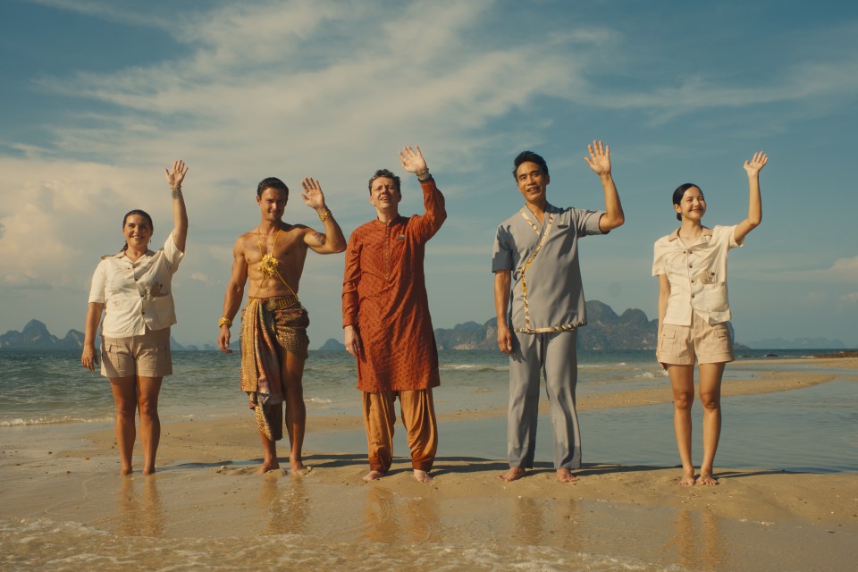 Five people on a beach waving.