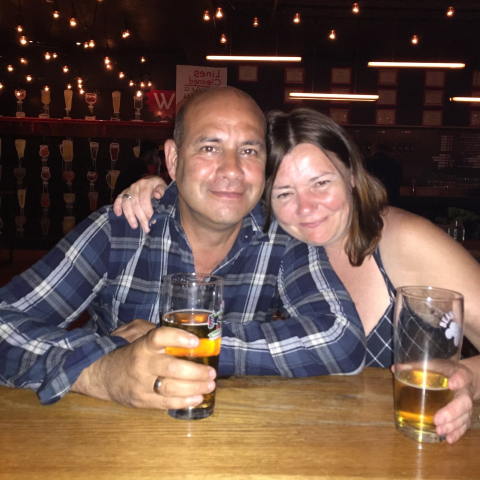 A man and woman sitting at a bar, each holding a beer.