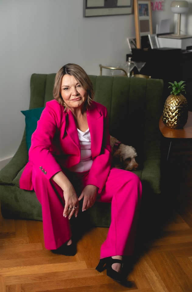 Woman in a pink suit sitting on a couch with a dog.