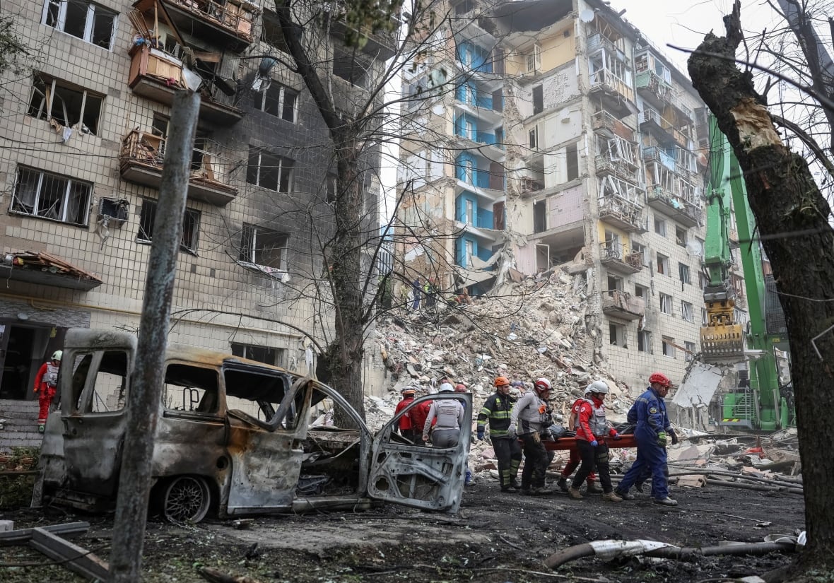 A bombed out building with medics carrying a stretcher.