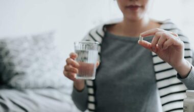 A woman holds a pill in one hand and a glass of water in the other.