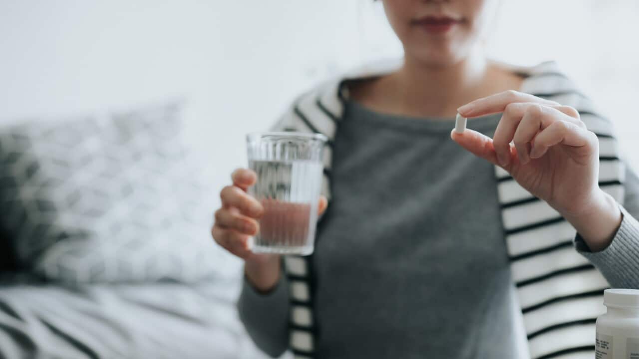 A woman holds a pill in one hand and a glass of water in the other.