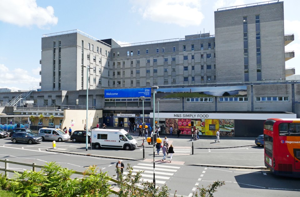 Hospital entrance with ambulance, shops, and public transport.