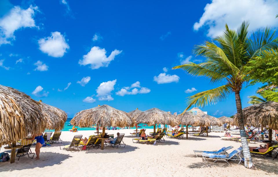 Beach scene with thatch umbrellas and people relaxing on lounge chairs.