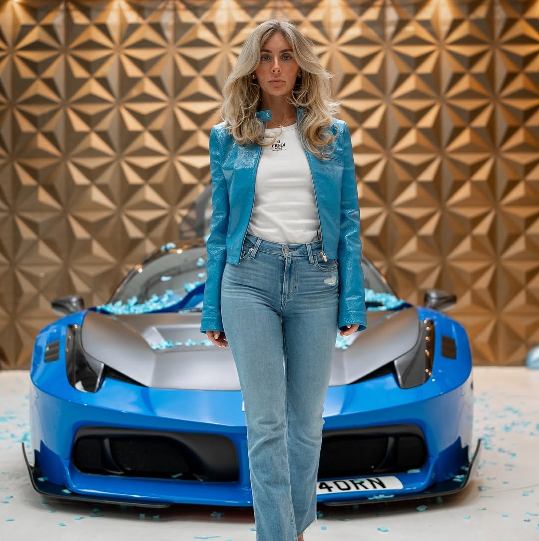 Woman in blue jacket standing in front of blue sports car.