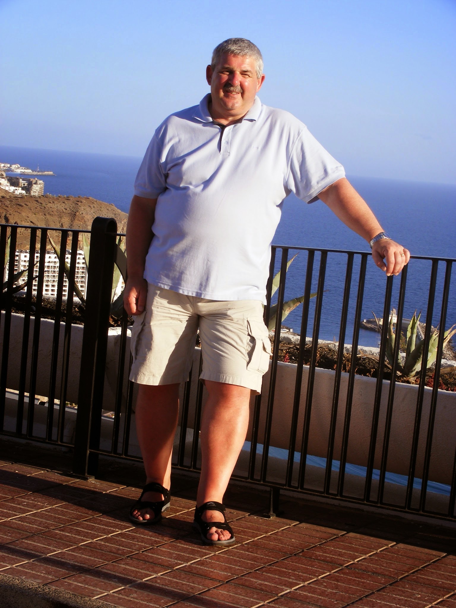 A man smiling and leaning on a railing overlooking the ocean.