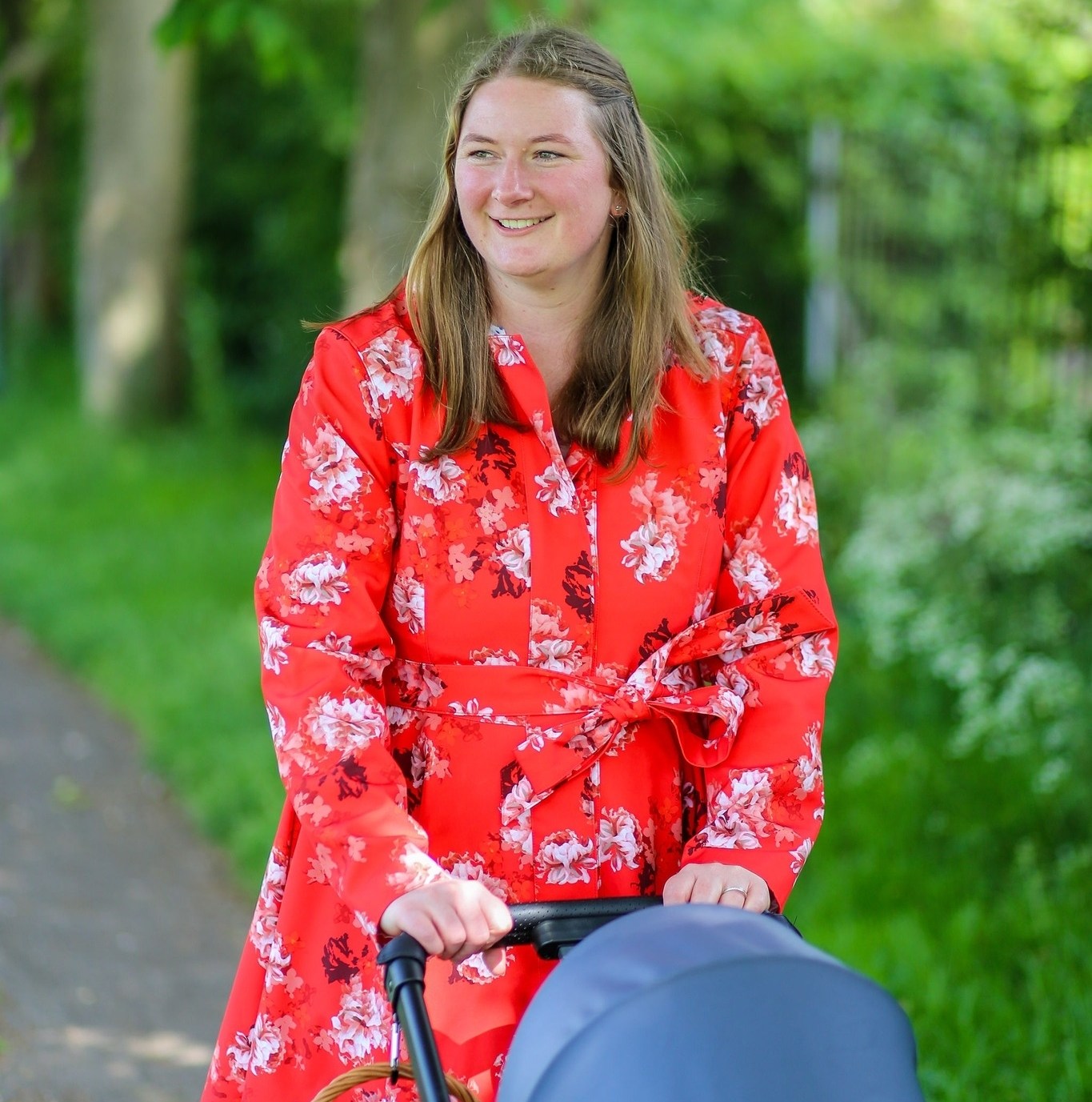 Woman in floral dress pushing stroller in park.