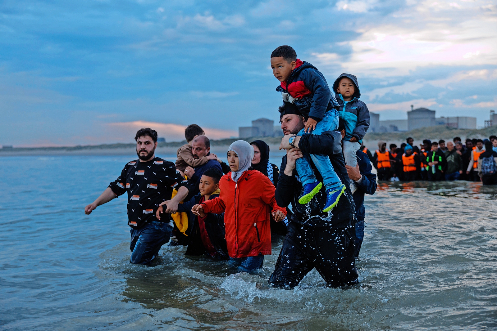 Migrant families wading into the sea to board a small boat.