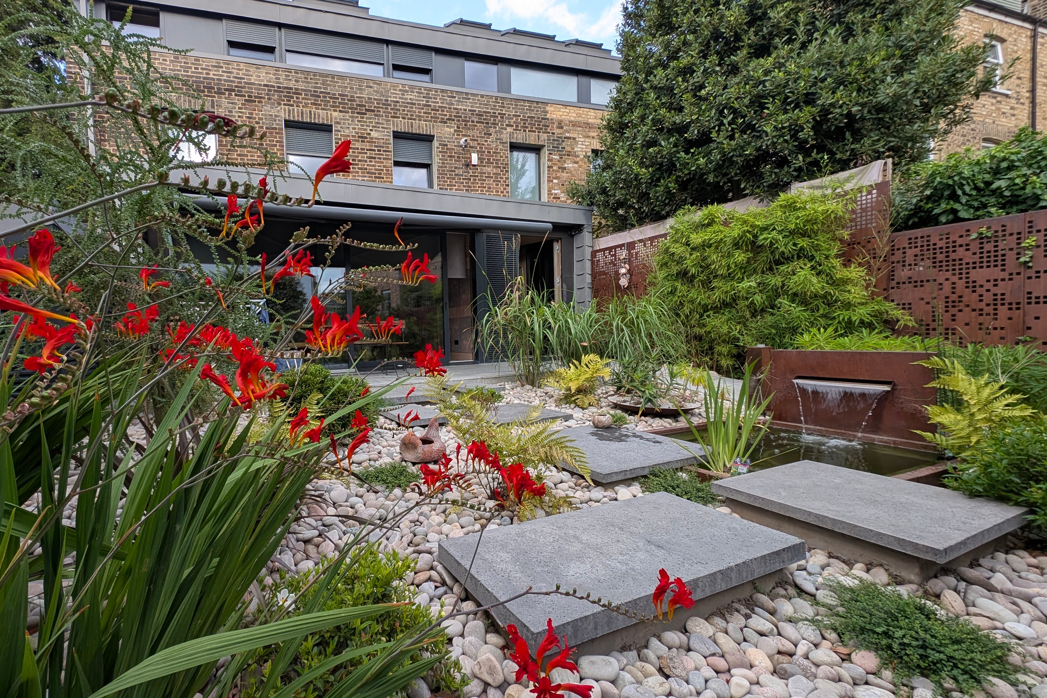 Garden extension with a water feature and red flowers.
