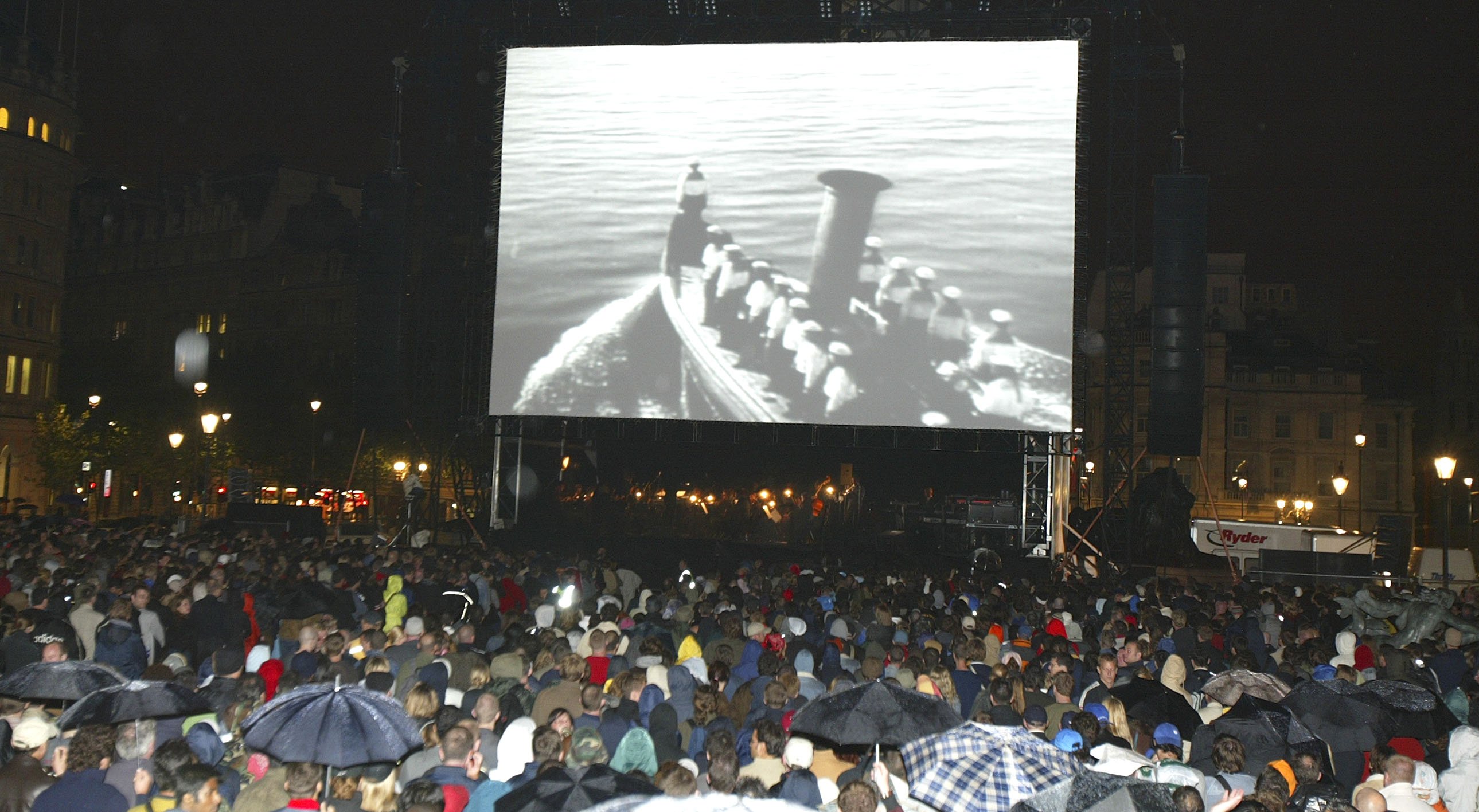 Large crowd watching a film screening outdoors at night.