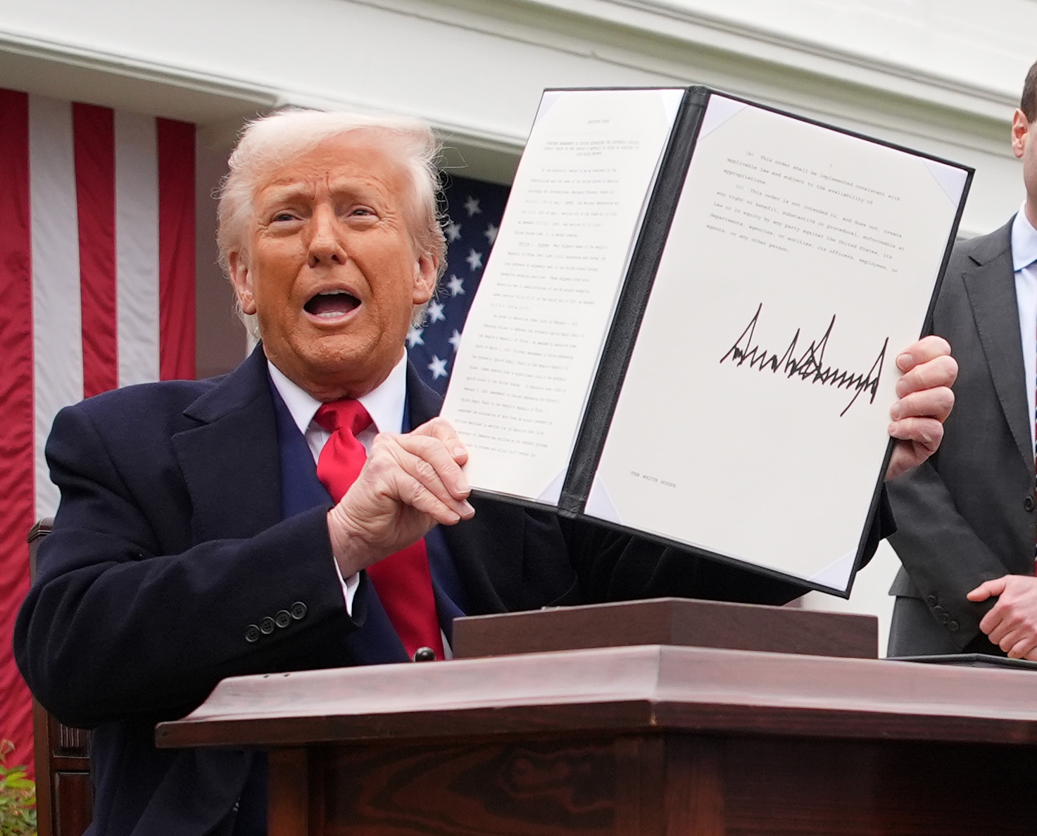 President Trump holding a signed executive order at a White House event.