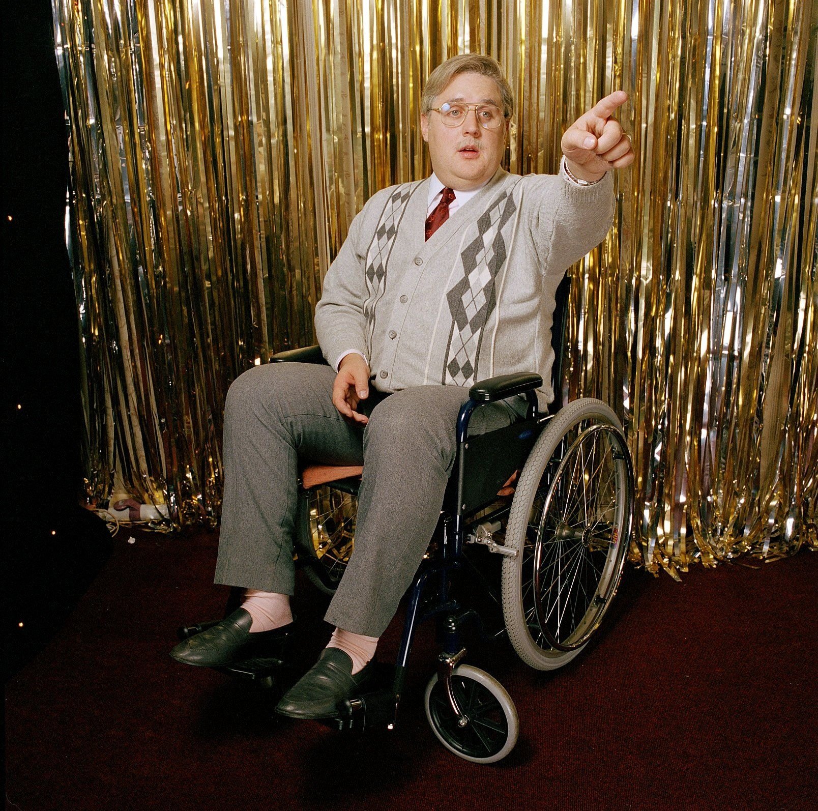 Peter Kay in a wheelchair, pointing.