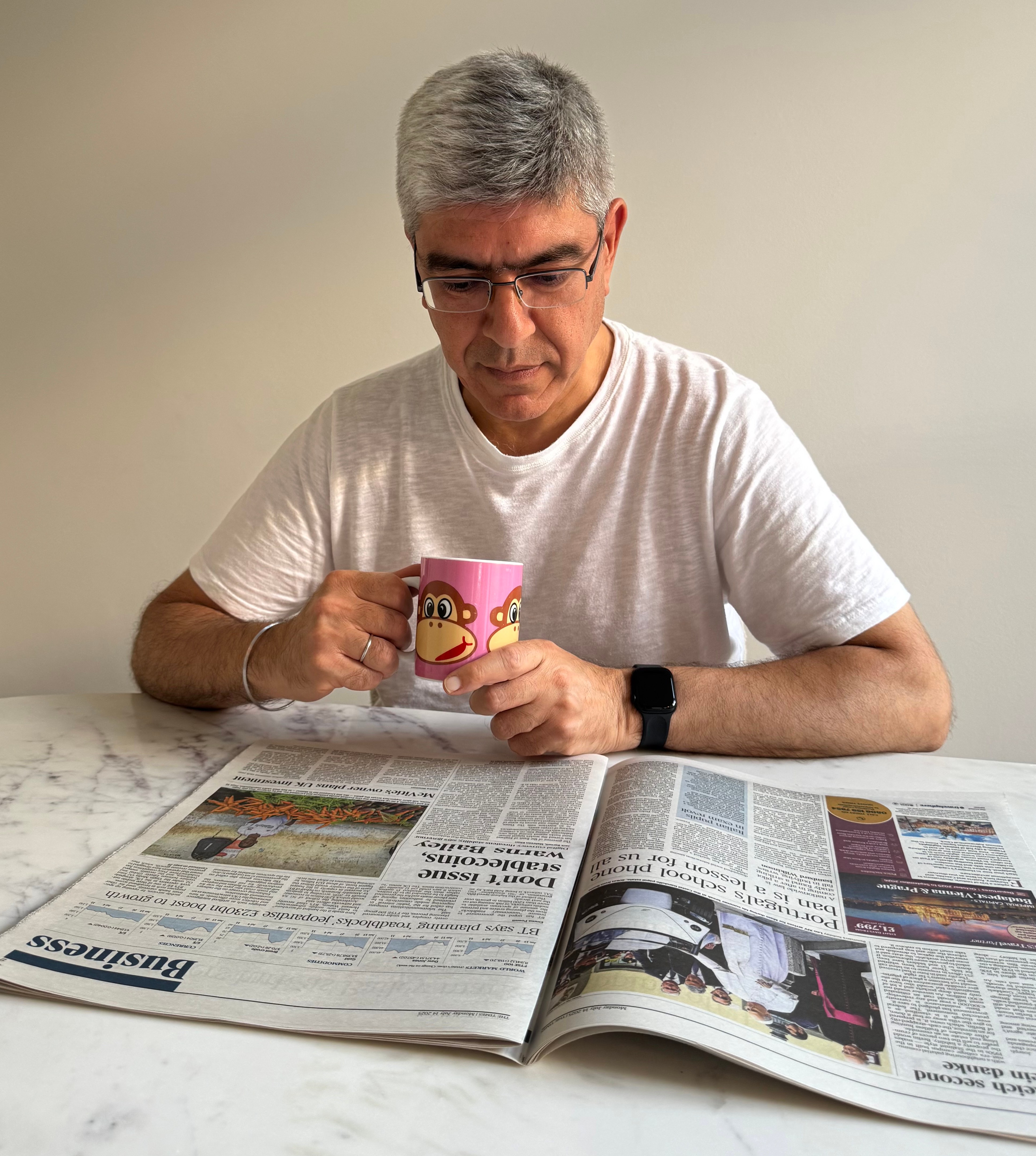 Man reading a newspaper while holding a mug.