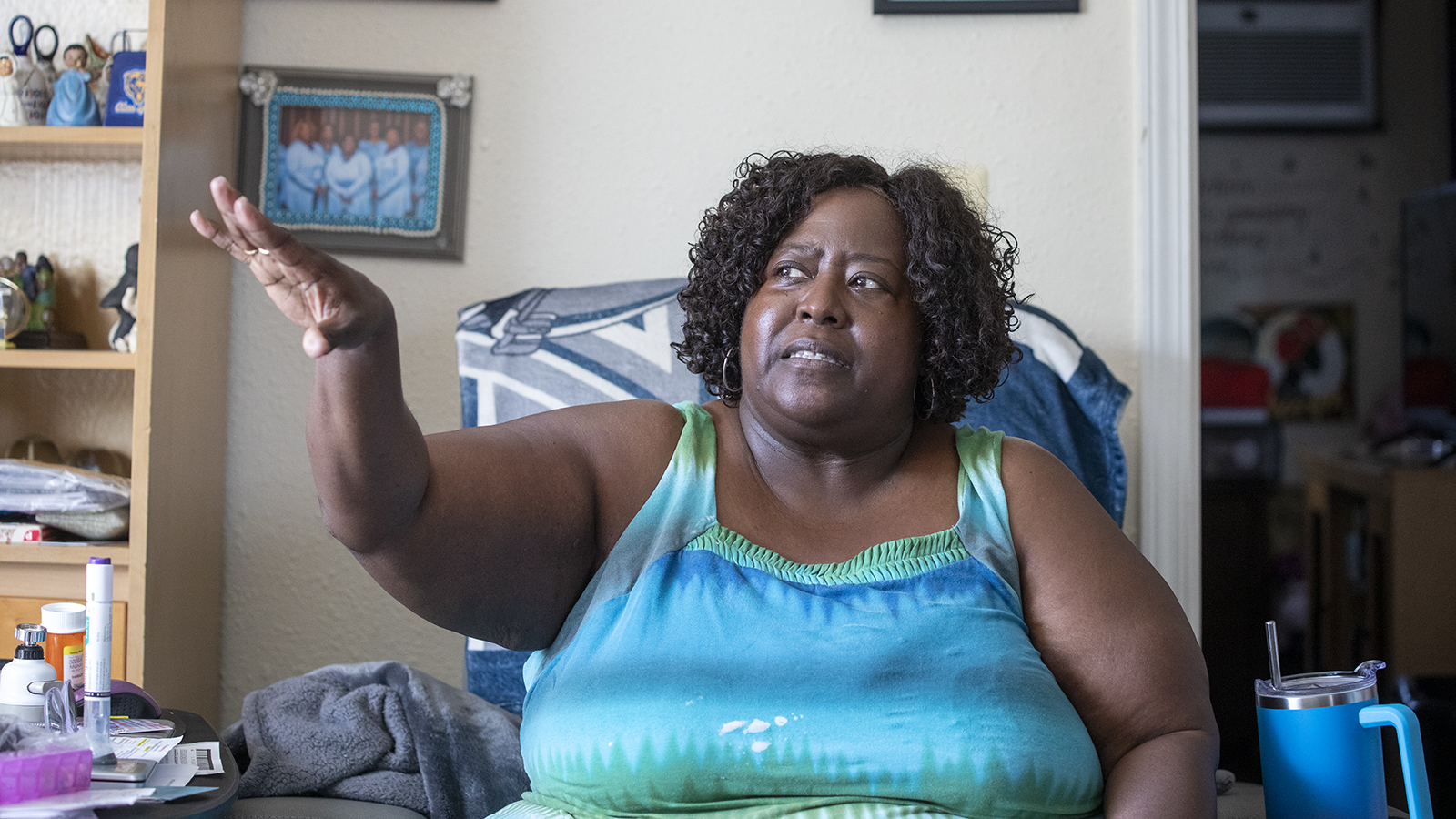 Kathleen Mosby, during an interview, gestures toward a bullet hole in her apartment window.