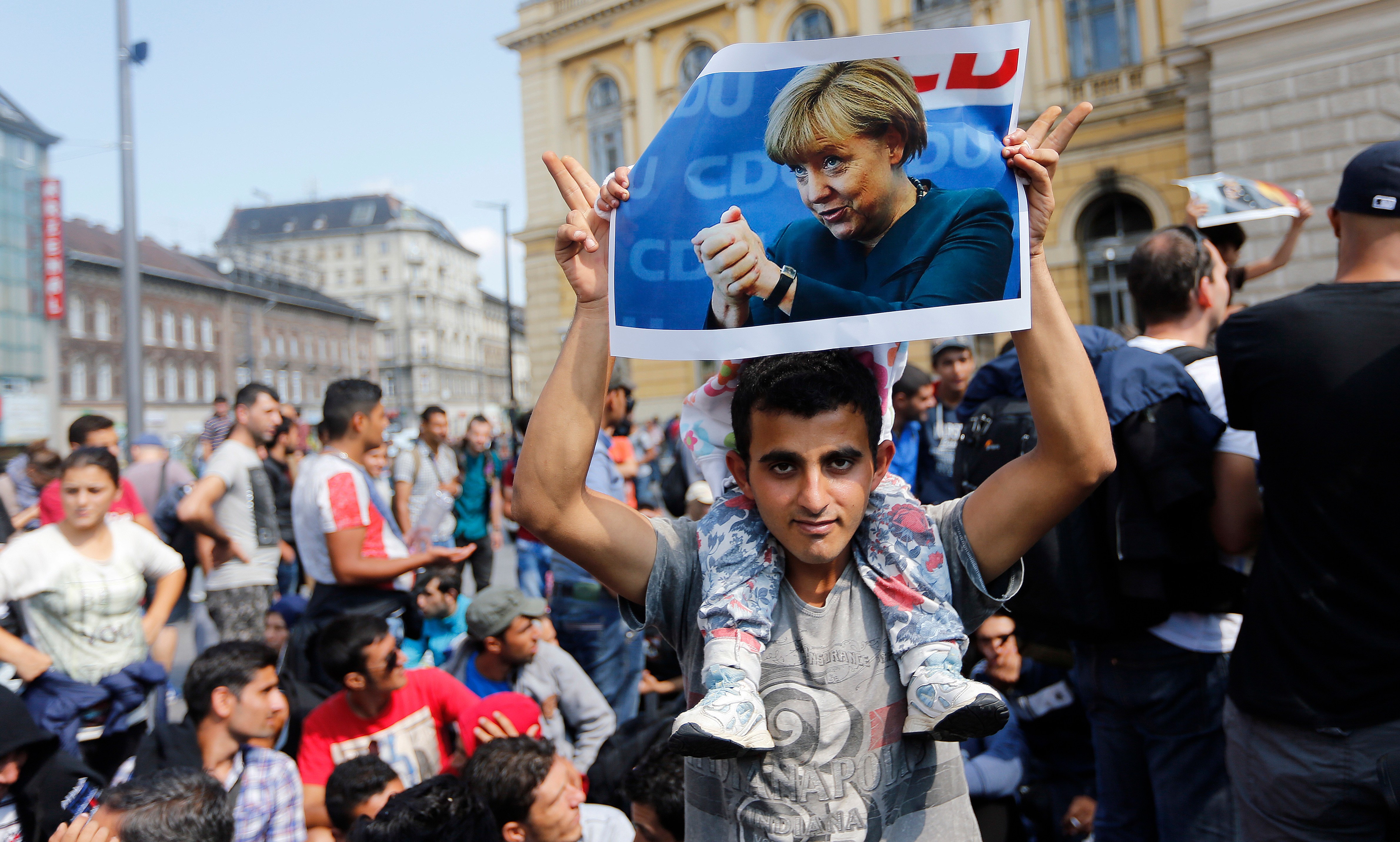 Migrant carrying a child and holding a poster of Angela Merkel.