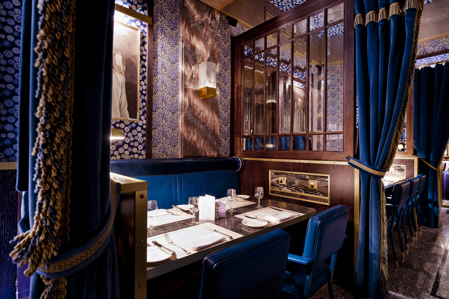 Photo of a restaurant booth with blue velvet curtains and a dark wood partition.