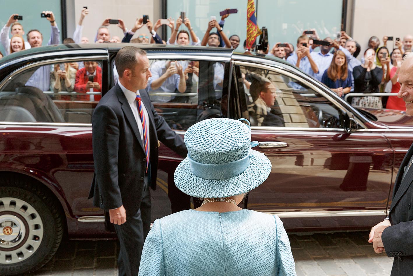 The Queen exiting a car, surrounded by photographers.