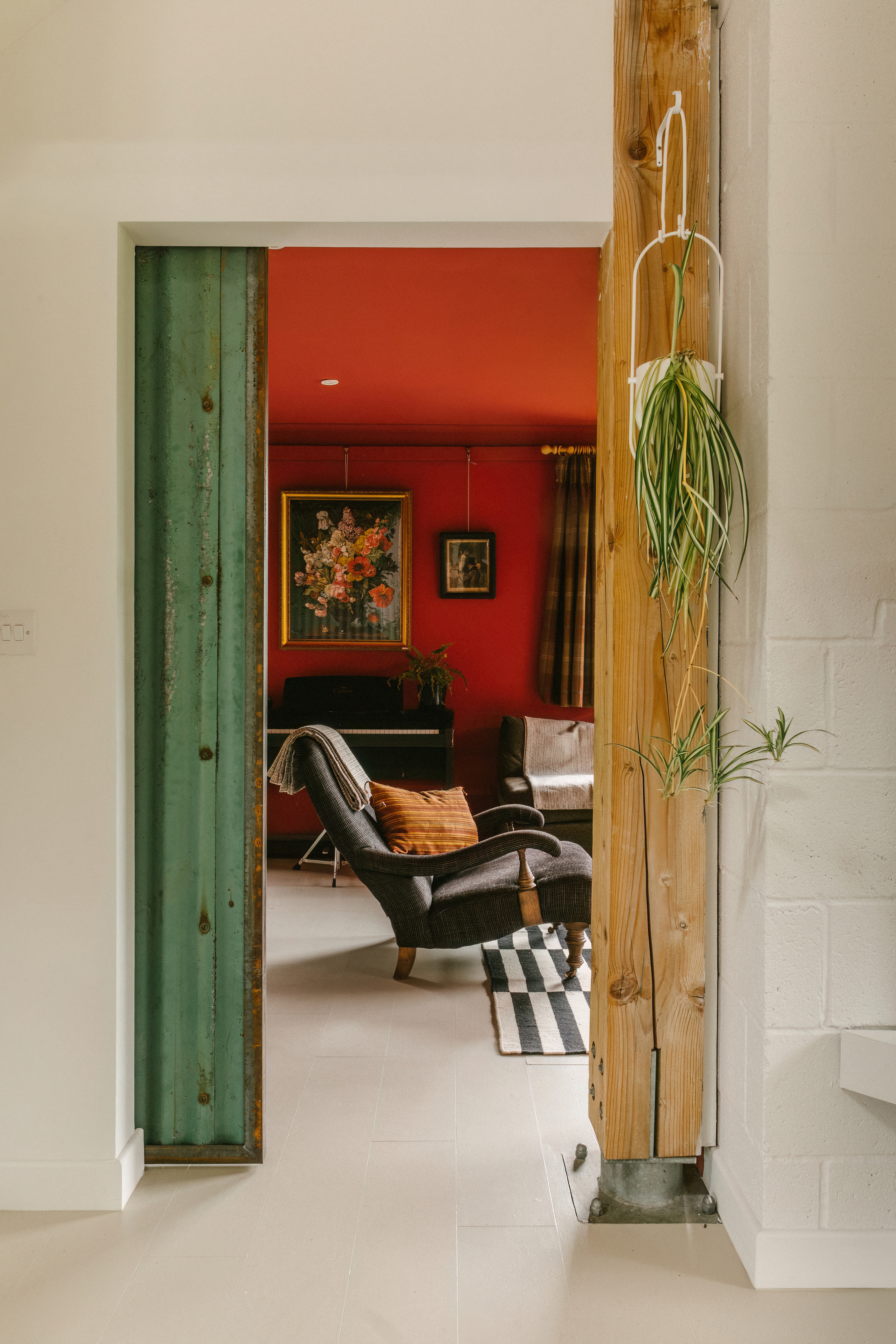 View of a living room with a red wall, armchair, and piano, seen through an open doorway.
