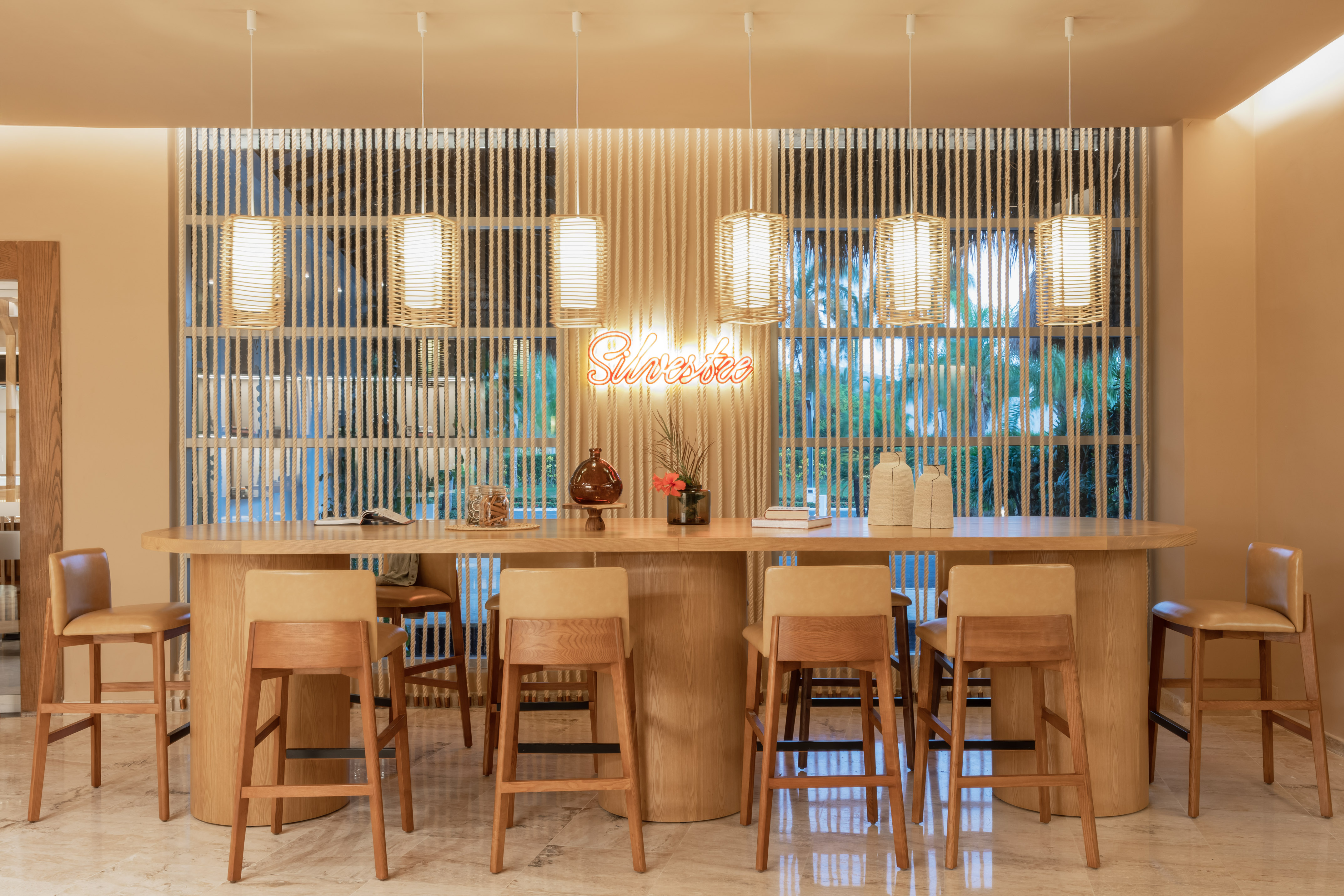Long wooden table with light beige stools and a neon sign that says "Silvestre".