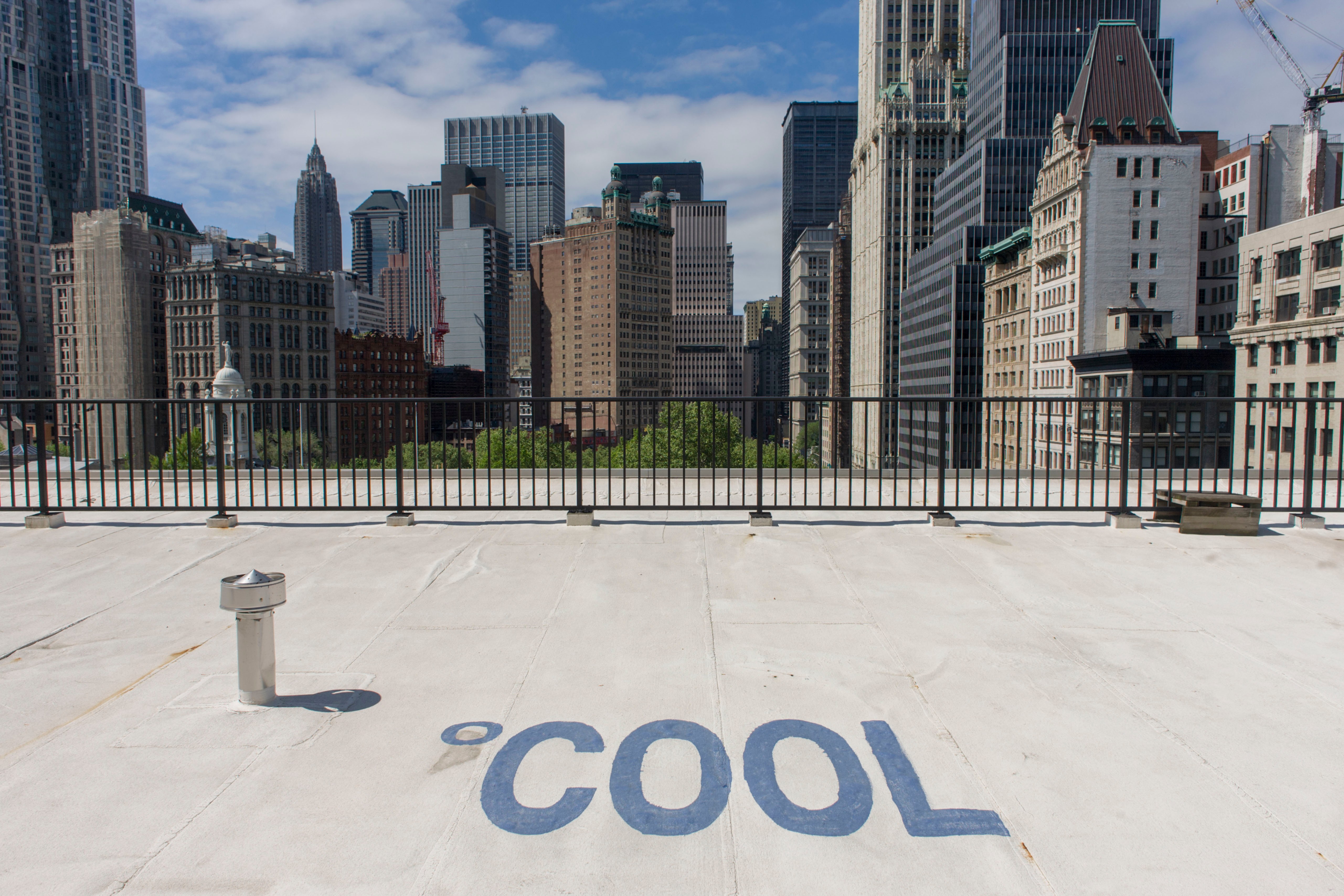 White rooftop in NYC with "COOL" painted on it, showcasing the cooling effect of the material. Skyscrapers are in the background.