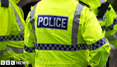 Image shows the back of a police officer's florescent yellow-green jacket. It has the word POLICE written in white capital letters on a blue background.