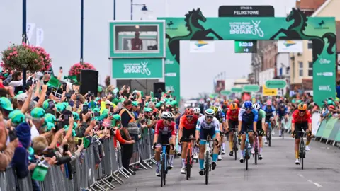 SWpix.com The Tour of Britain race finishing in Felixstowe in 2024. Bike riders race down a road with spectators cheering them on from either side of the road.