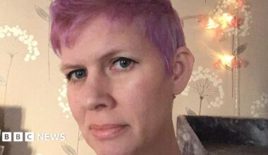 Maddie Walker with a fair complexion, purple hair and dark eyeliner looking at the camera with a soft smile.