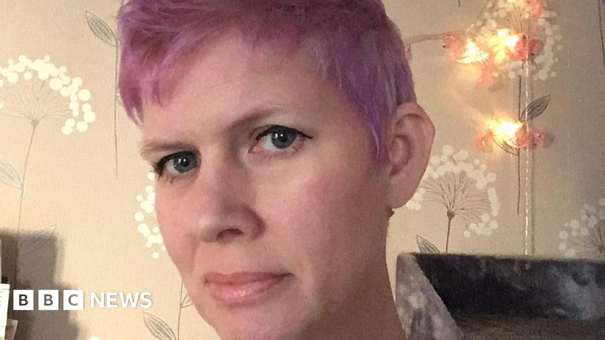 Maddie Walker with a fair complexion, purple hair and dark eyeliner looking at the camera with a soft smile.