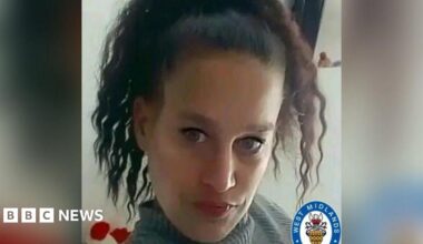 A woman with curly dark hair and black eyeliner, wearing a grey turtleneck, looks at the camera. The West Midlands Police logo is at the bottom right of the picture.