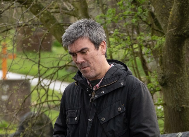 Cain looks sad as he stands in a graveyard on Emmerdale