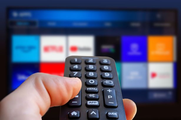 A close-up of a remote pointed at a TV showing a blurred screen full of streaming options.