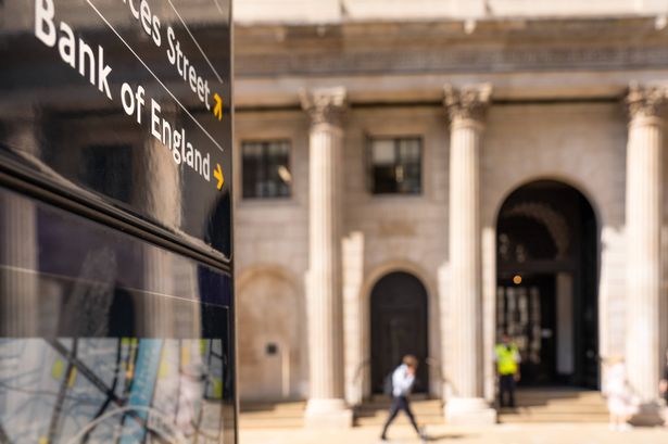 Close-up on a sign for the Bank of England, with a pedestrian passing the institution's main entrance in the background.