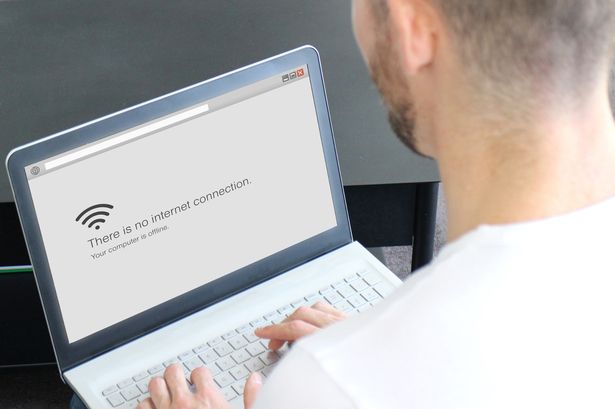 Looking over the shoulder of a man on a laptop with a screen that has a WiFi symbol and the words 'there is no internet connection'