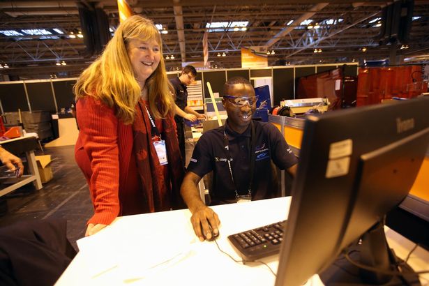 A woman leaning onto a desk while a man looks at a computer