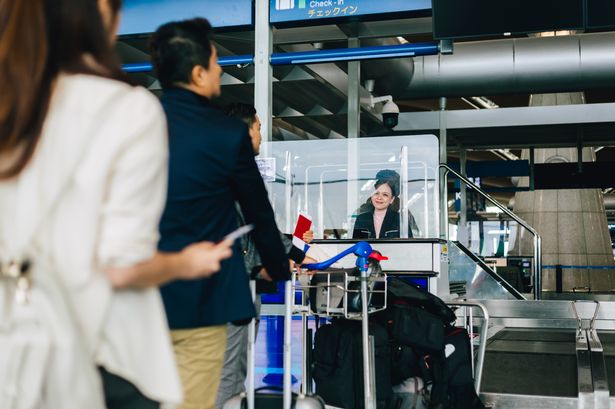 Group of passengers with luggage trollies standing in line at airport check in counter.