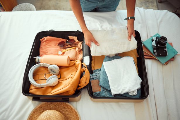 Woman packs clothes into open suitcase