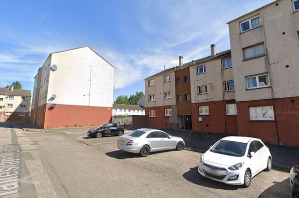 An image of a residential street with cars parked outside three-storey blocks.