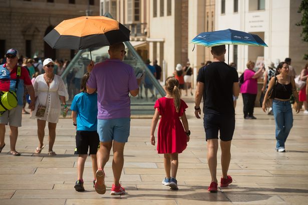 Tourists hold umbrellas to protect themselves from the sun as they walk during a hot summer day in Malaga, Spain, on 05 August, 2025