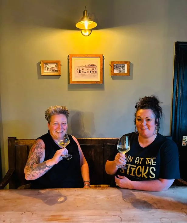 Two women smiling with wine at a table 