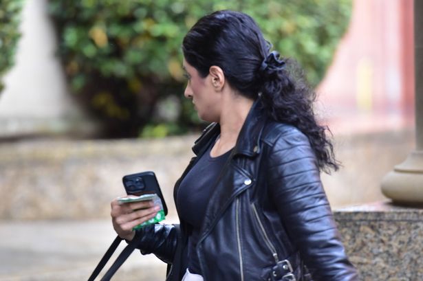 An image of a dark-haired woman wearing a leather jacket, walking and looking away from the camera.
