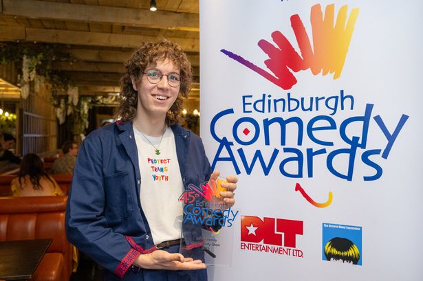 An image of a woman with curly brown hair and glasses, holding a glass trophy and posing next to a banner reading "Edinburgh Comedy Awards".