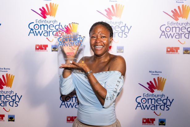 An image of a Black woman with cropped dark hair, smiling as she holds up a glass trophy.