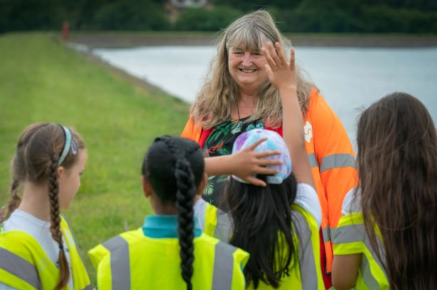 Woman in hi-vis jacket waves at children