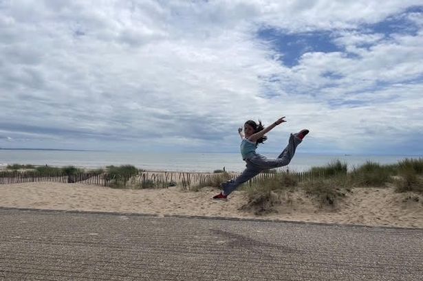 Dakota jumping in the air, striking a dance pose mid-air on the Swansea promenade. Swansea bay is visible in the background.