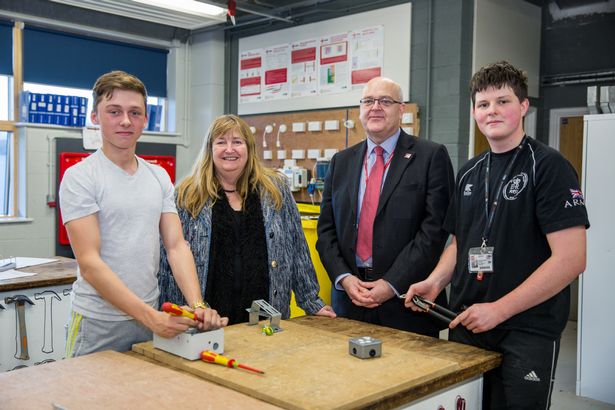 Two adults stood with students at a college in a workshop