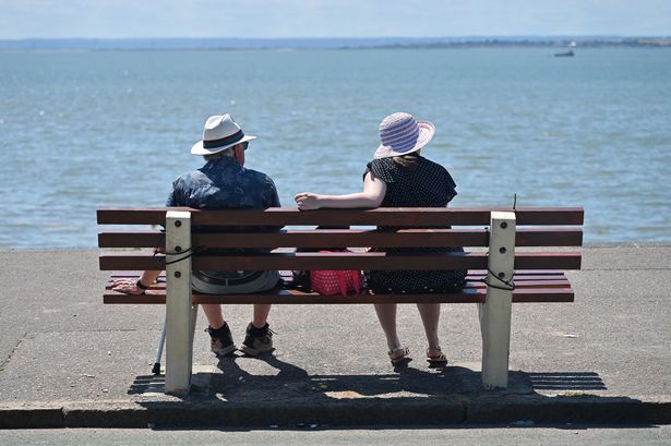 : Two people wear sun hats as they sit on a bench and look out to sea during the recent hot sunny weather on Westcliff beach 