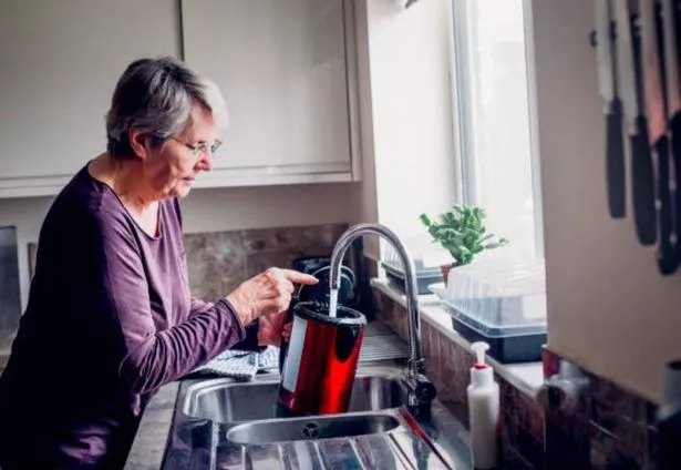 Elderly woman filling up a red kettle with water