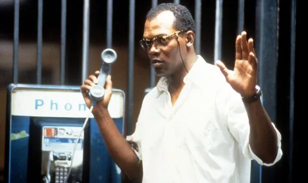 A man in glasses holds a phone and his hands in the air